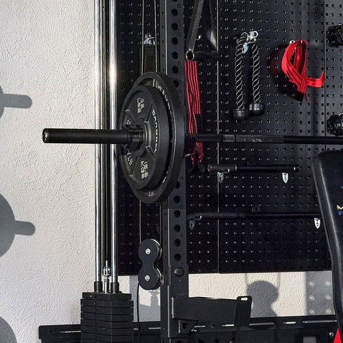 Barbell with weight plates on a squat rack against a pegboard wall in a gym setting.