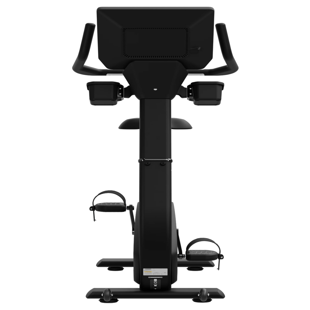 A black upright exercise bike with a large digital display screen on the back, armrests, and foot pedals, shown from a front-facing perspective against a solid white background.