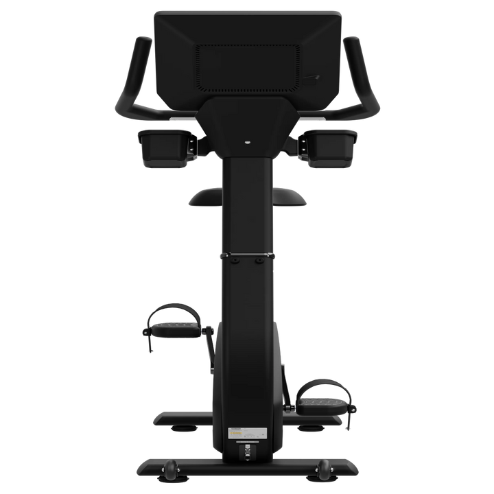 A black upright exercise bike with a large digital display screen on the back, armrests, and foot pedals, shown from a front-facing perspective against a solid white background.