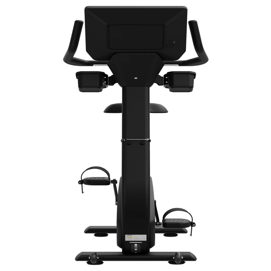 A black upright exercise bike with a large digital display screen on the back, armrests, and foot pedals, shown from a front-facing perspective against a solid white background.