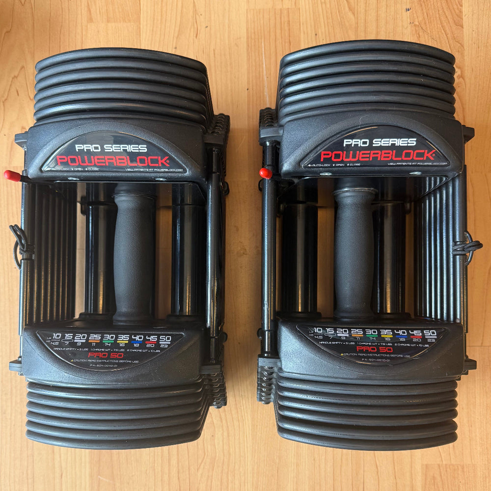 Two black PowerBlock Pro Series Pro 50 hand weights placed side-by-side on a light wood floor.