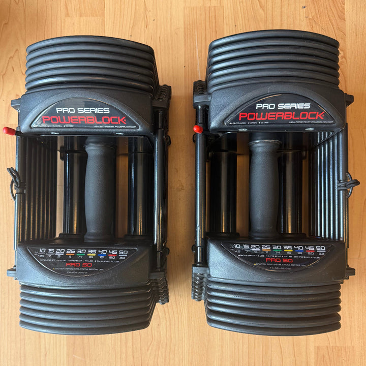 Two black PowerBlock Pro Series Pro 50 hand weights placed side-by-side on a light wood floor.