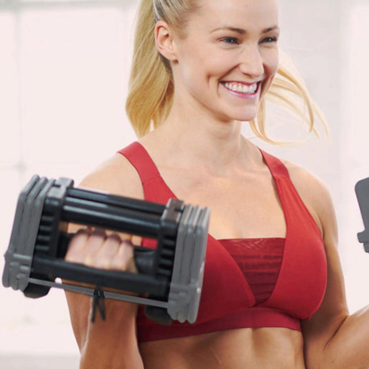 Woman in red sports bra and shorts using adjustable dumbbells against a light background