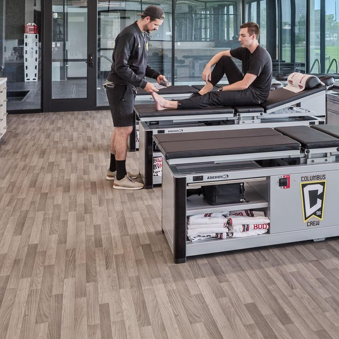 Two men working on a piece of exercise equipment in a modern facility with large windows.