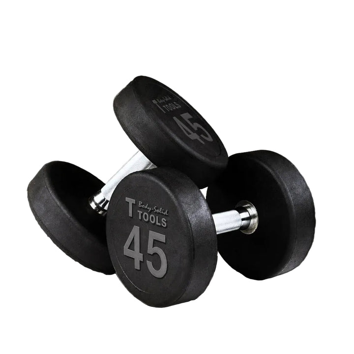 Two black rubber-coated dumbbells with silver metal handles, each marked 45 lbs, displayed on a concrete floor against a gray wall.