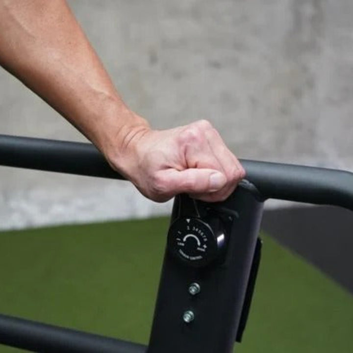 Hand gripping a black handlebar with a control knob on a green surface.
