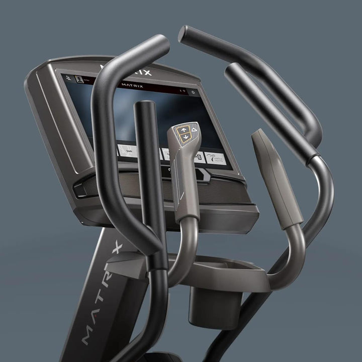 Close-up of a Matrix elliptical trainer showing the console, handrails, and lower handlebar against a dark gray background.