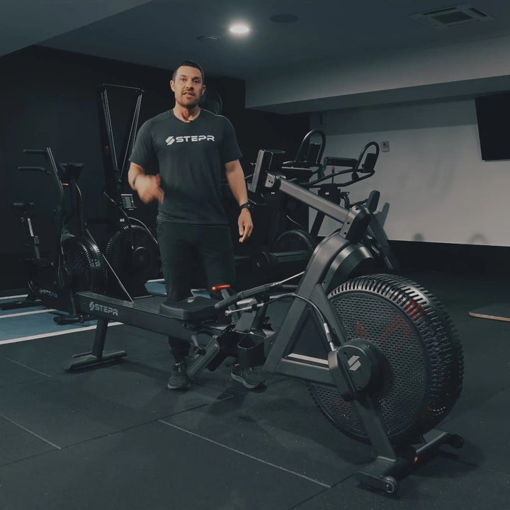 Man standing next to a rower in a gym setting