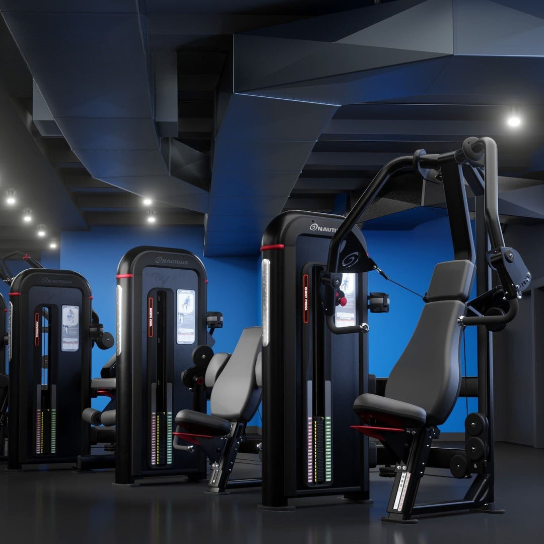 A row of modern cable pulley strength training machines in a dark gym with blue accent walls and ceiling lights.