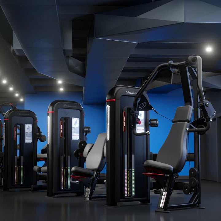 A row of modern cable pulley strength training machines in a dark gym with blue accent walls and ceiling lights.