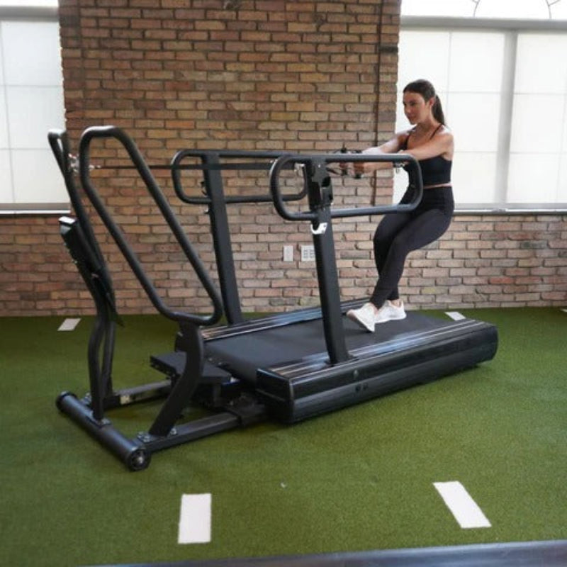 Woman exercising on a treadmill in a gym setting with brick walls and green flooring.