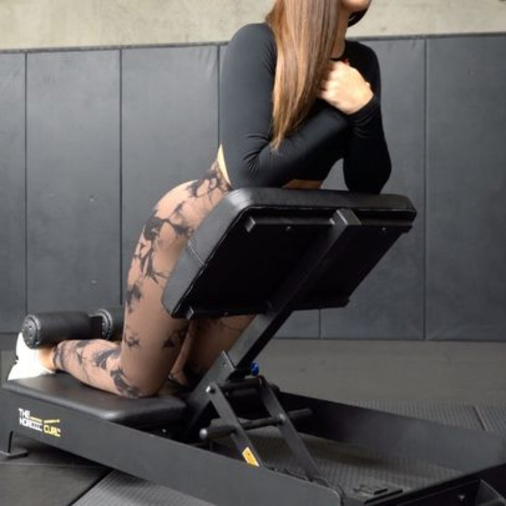 Person using a black exercise machine against a dark tiled wall.