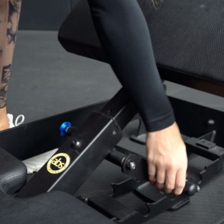 Person adjusting a black exercise machine with visible tattooed legs.