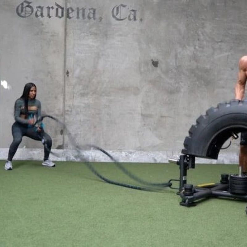 Two people working out with a tire and resistance band in a gym setting.