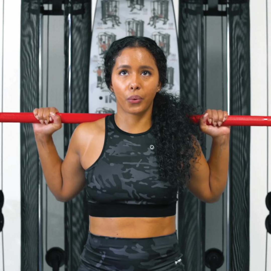 Woman in black athletic wear performing pull-ups on a red bar.