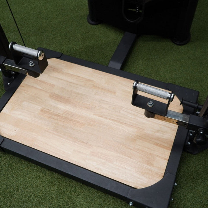 Wooden base plate attached to a piece of gym equipment on a green floor.