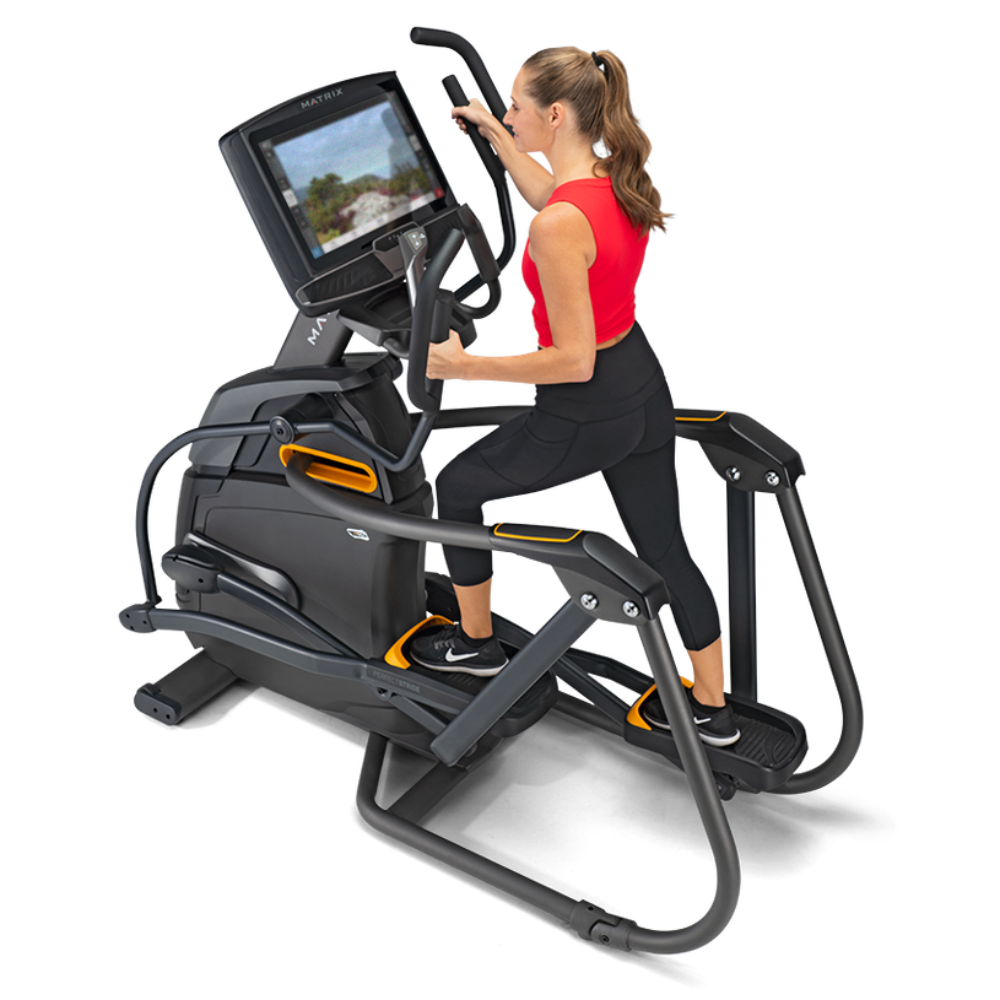 A woman in a red tank top and black leggings is using a black and gray elliptical trainer with an attached screen, shown on a clean white background.