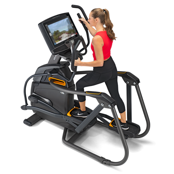 A woman in a red tank top and black leggings is using a black and gray elliptical trainer with an attached screen, shown on a clean white background.
