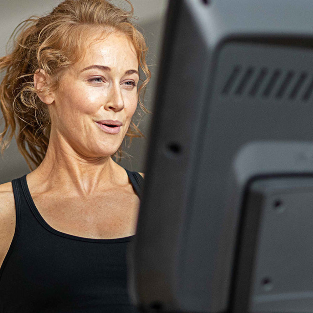 Woman in a black tank top standing next to a piece of gym equipment.