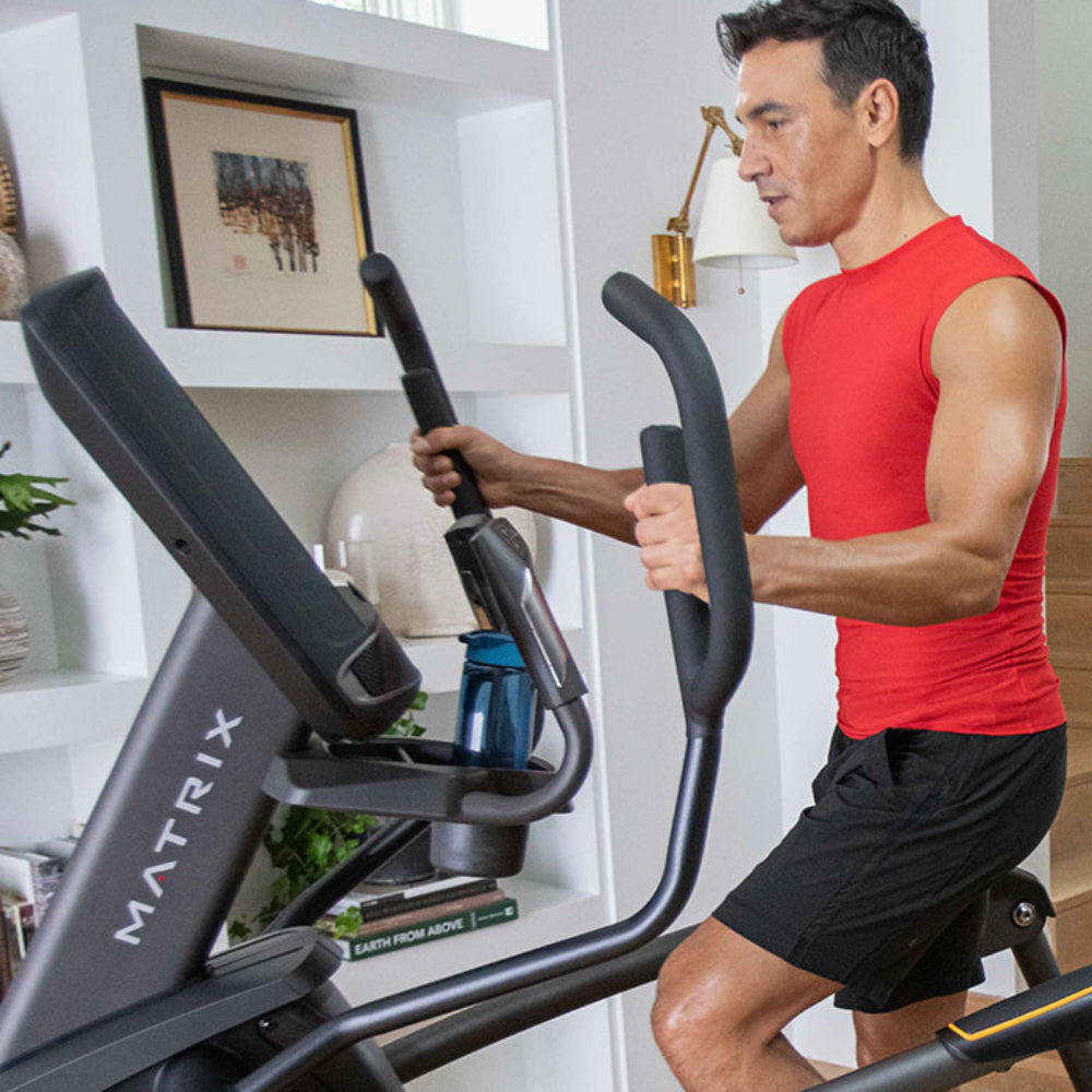 Man and woman exercising on a Matrix elliptical machine in a home setting.