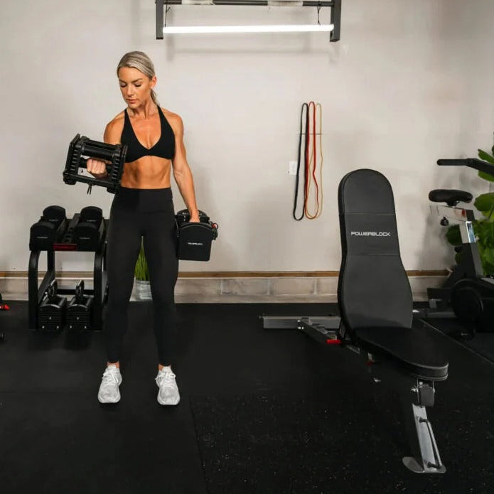 Woman exercising with dumbbells in a home gym setting.